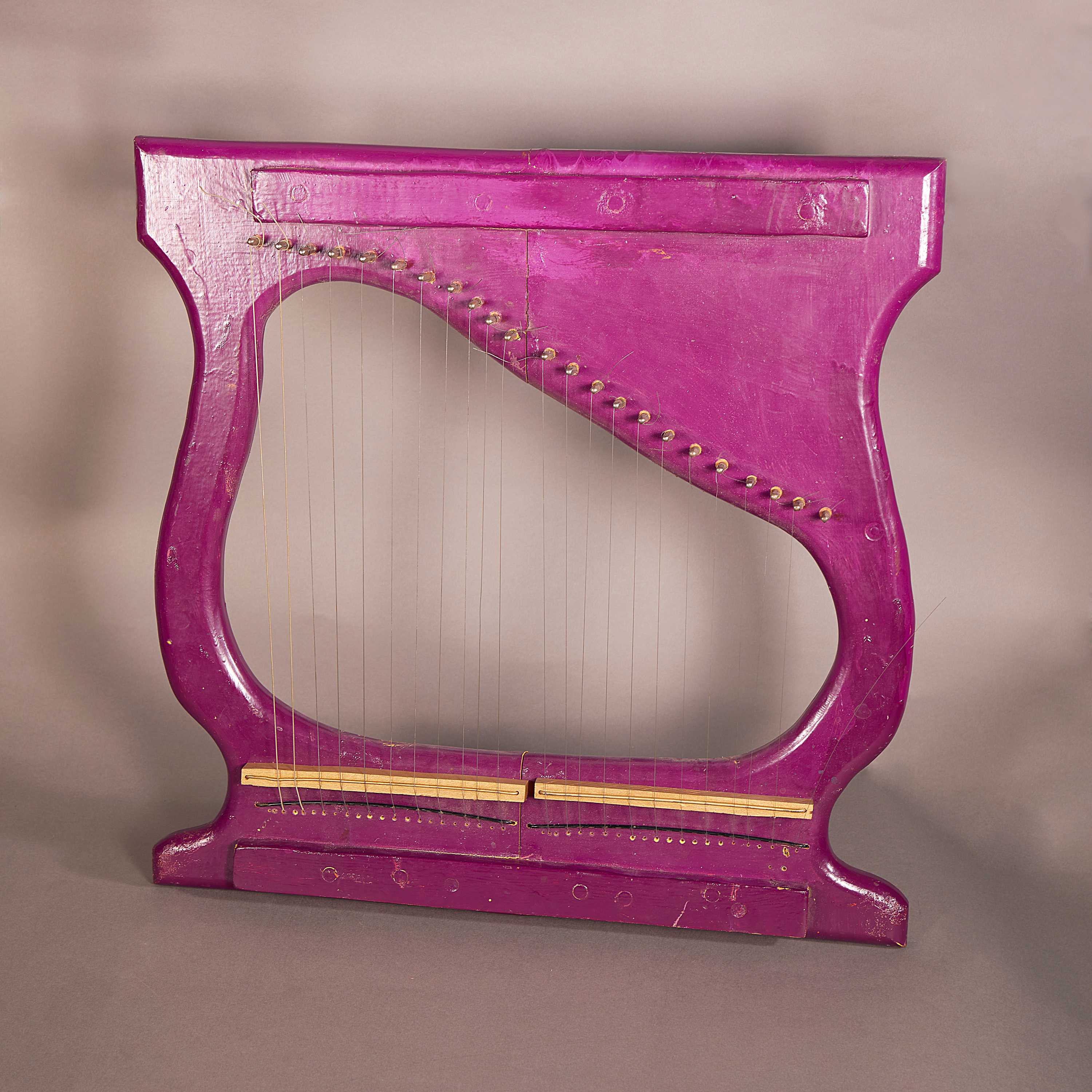 A vibrant pink harp has about 20 plus strings. It sits in front of a plain background.