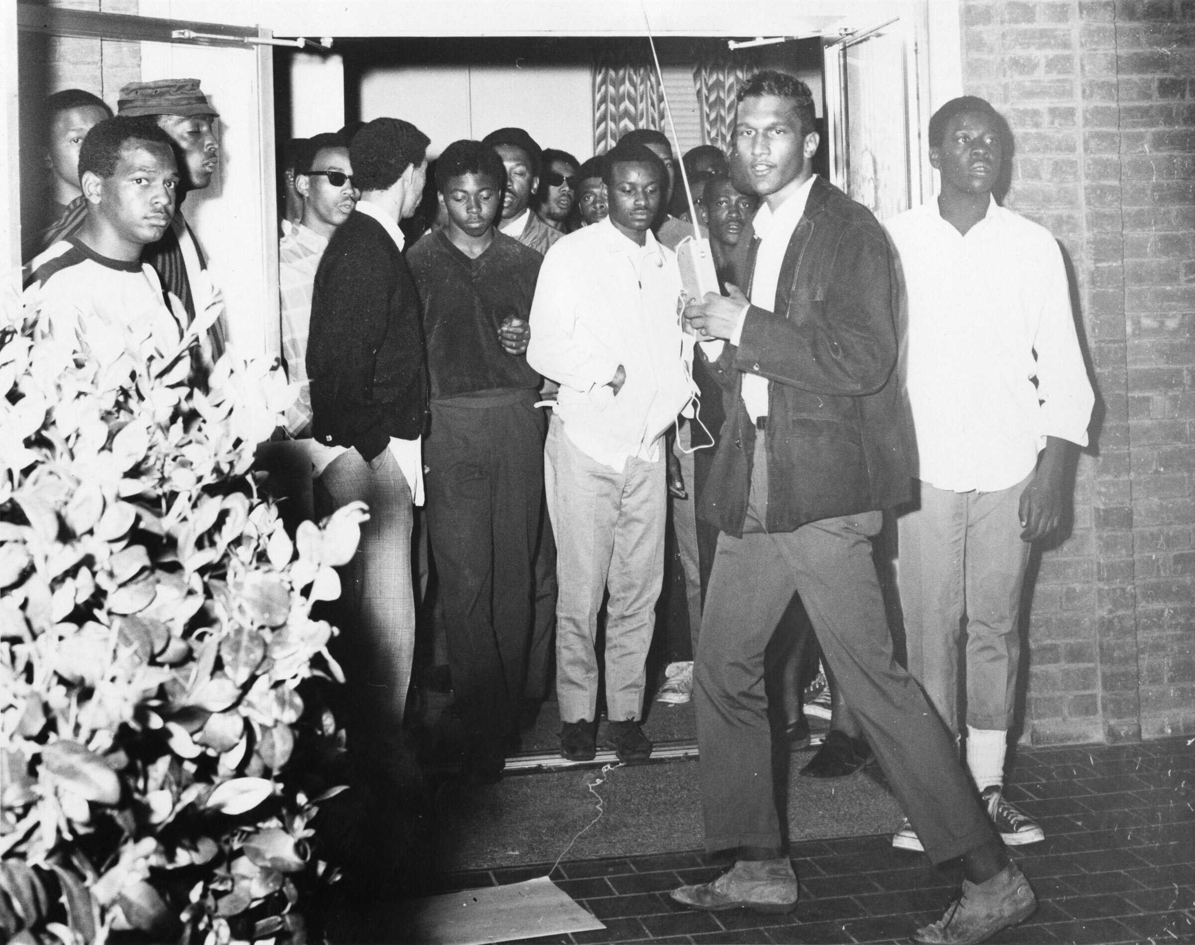A black and white photo of a group of people standing in the doorway of a building.