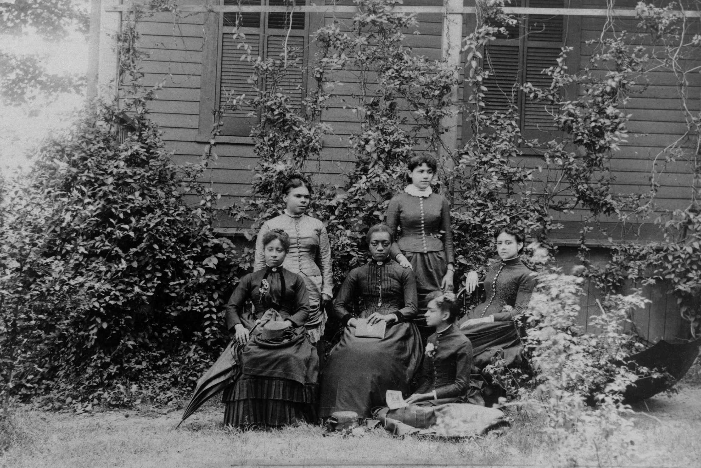 A black and white photo of 6 students sitting in front of a schoolhouse. It is labeled 'Graduates of 1887'.
