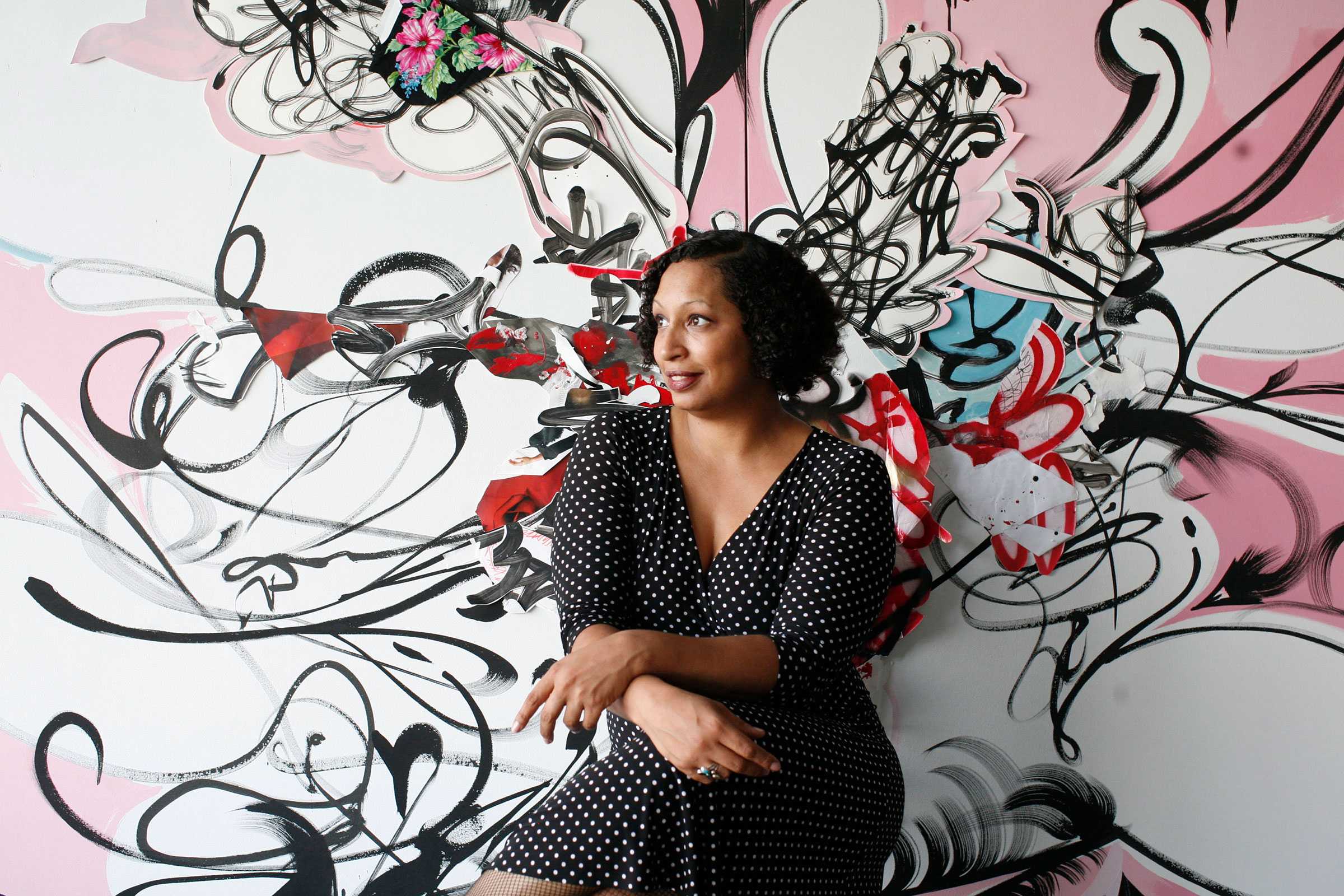 Person sitting in front of an abstract mural with bold black, red, and pink brushstrokes, creating a dynamic background.