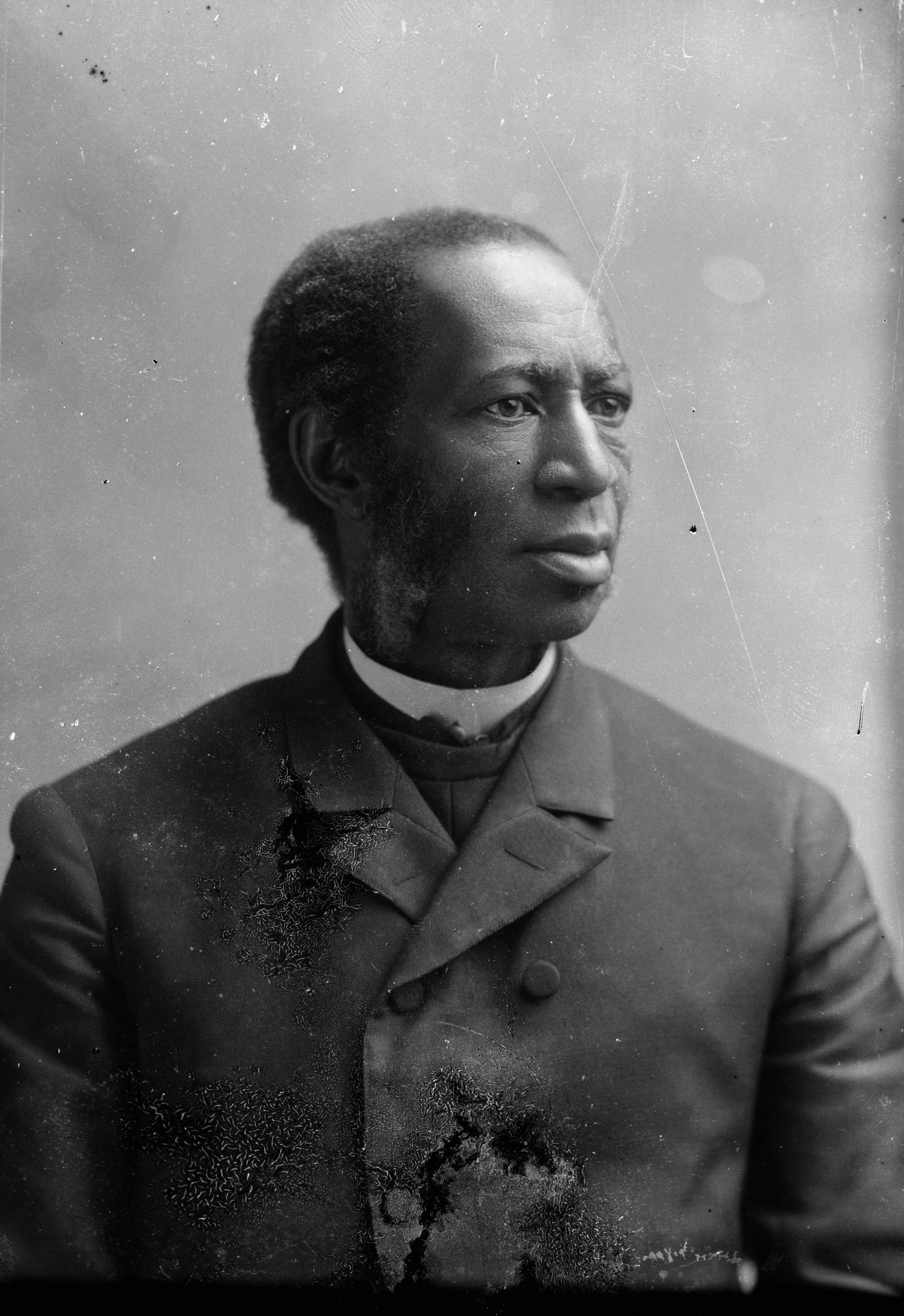 A worn black and white photo of Reverend Richard Harvey Cain. He is looking off camera in a suit.