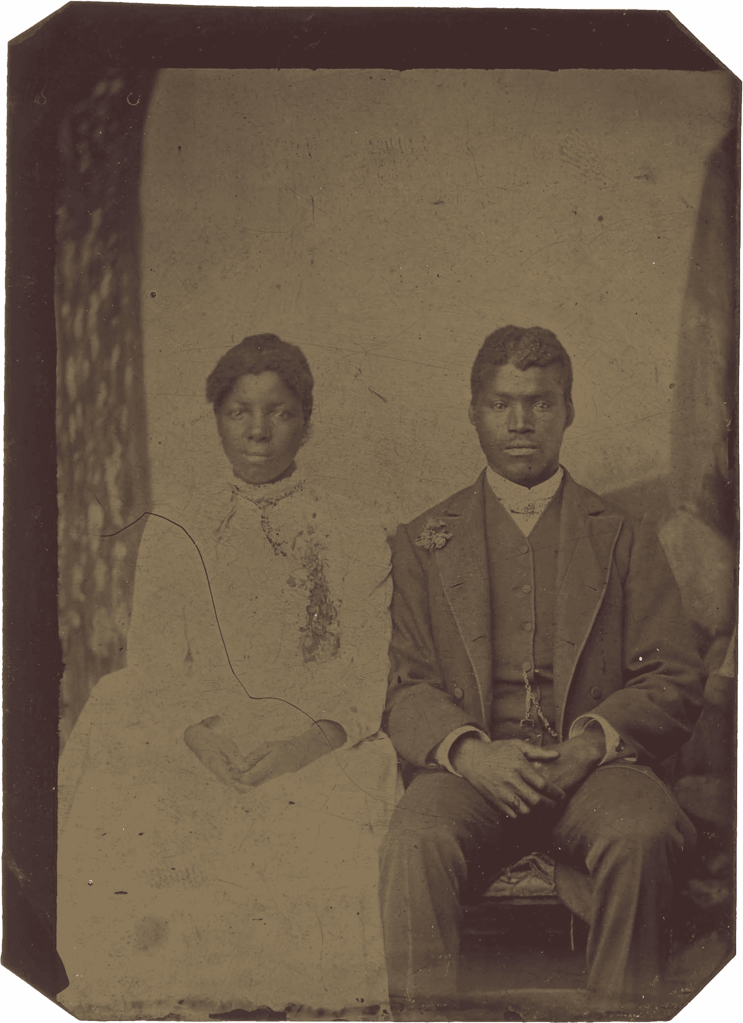 Sepia-toned photograph of a seated couple, both wearing formal attire, against a plain backdrop.