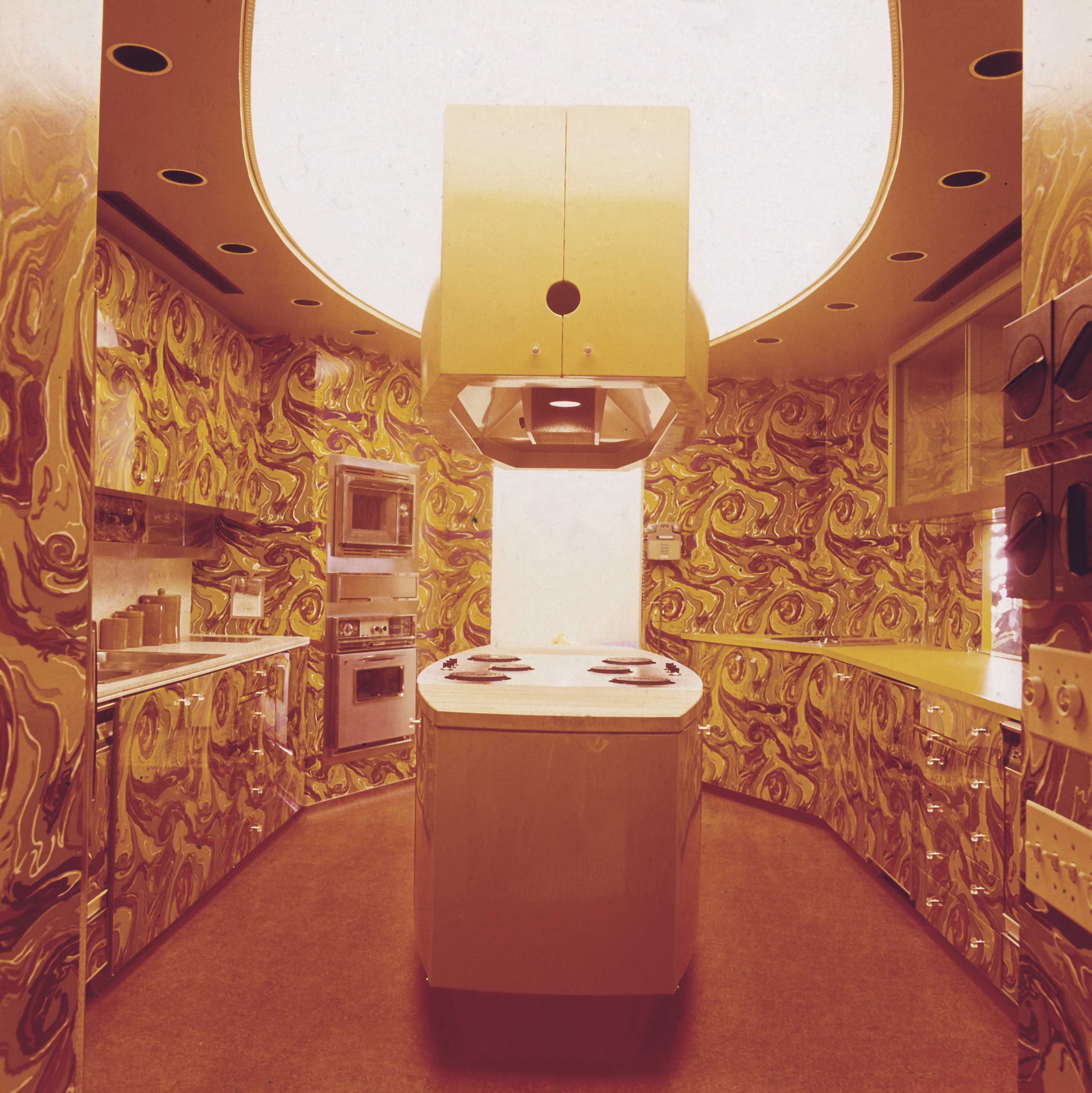 A sepia tone photo of the Ebony Test Kitchen. The oval shape island sits at the center of the of the kitchen.