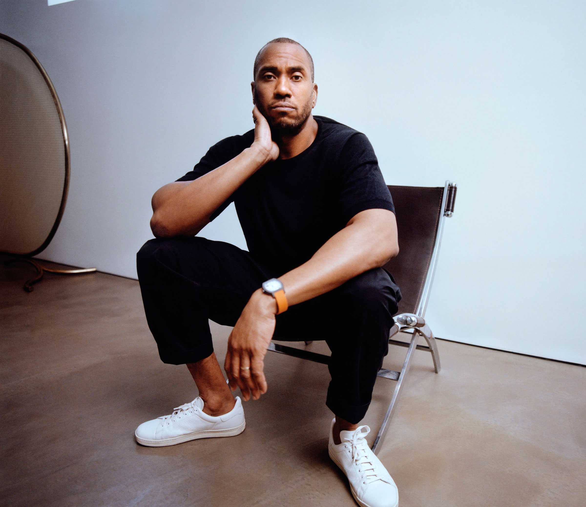 Person seated casually on a chair, looking directly at the camera, with a neutral expression.