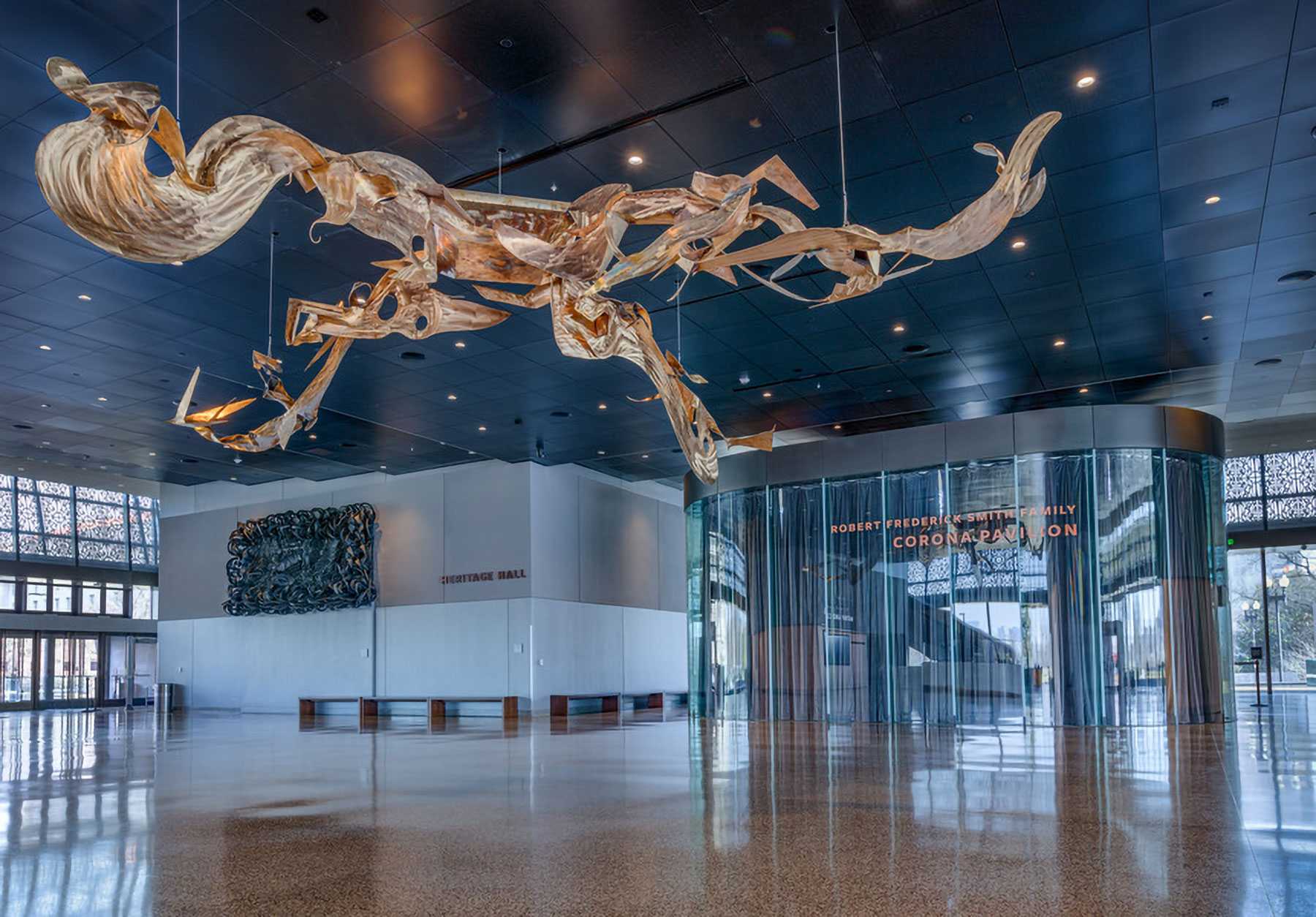 Sculpture suspended from the ceiling in a large, modern hall with "Heritage Hall" and "Corona Pavilion" signs visible.
