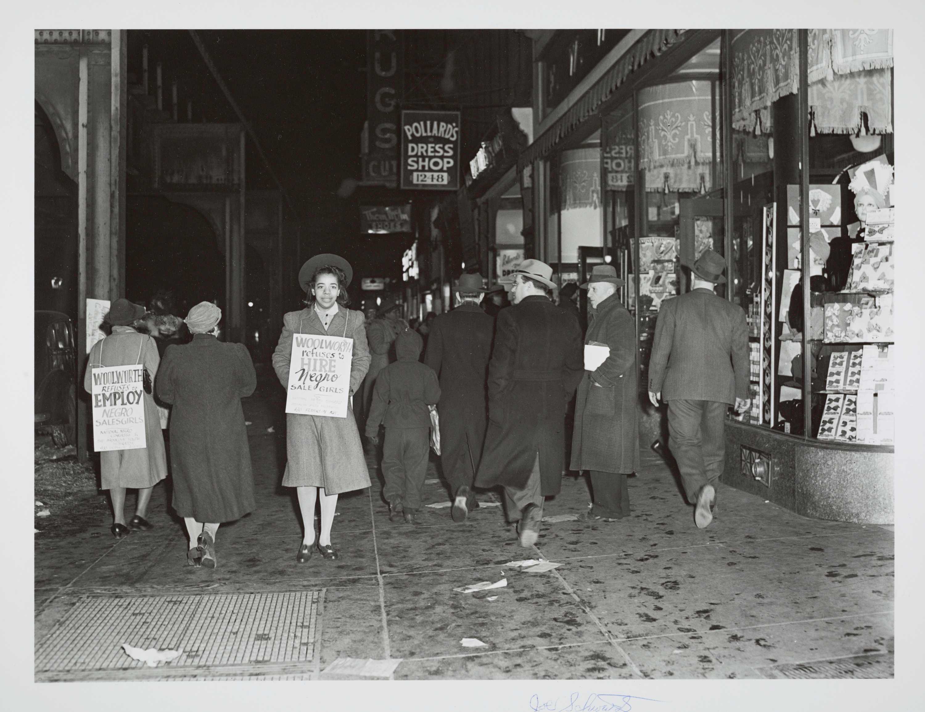 A black-and-white photograph of two girls protesting in front of an F. W. Woolworth's store. The pair wear signs announcing that "Woolworth refuses to hire Negro sale girls."