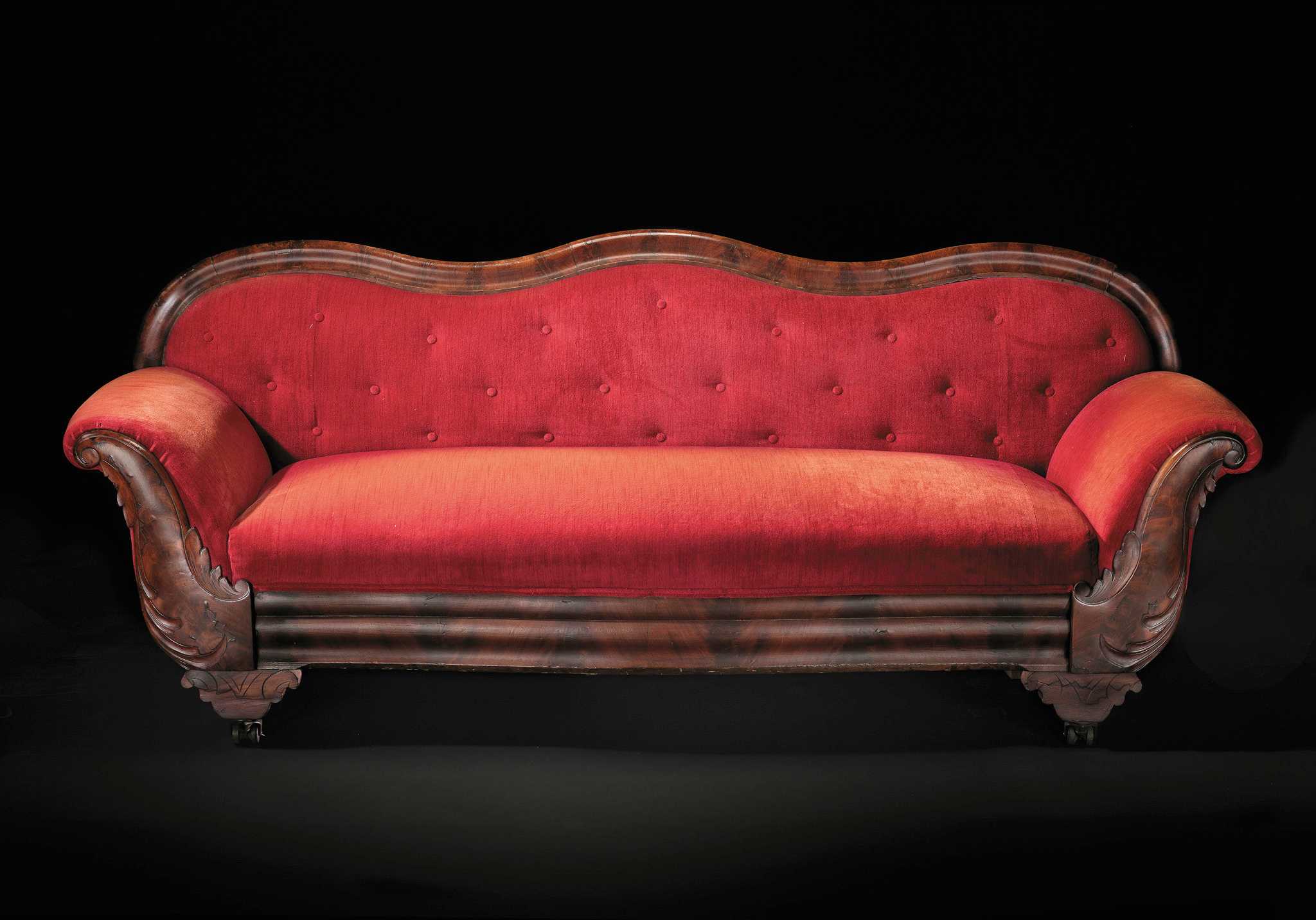A Late Classical mahogany sofa, upholstered in red, with serpentine, tufted back and wing scroll arms, crotch mahogany decorative veneers on crest, arms, and apron.