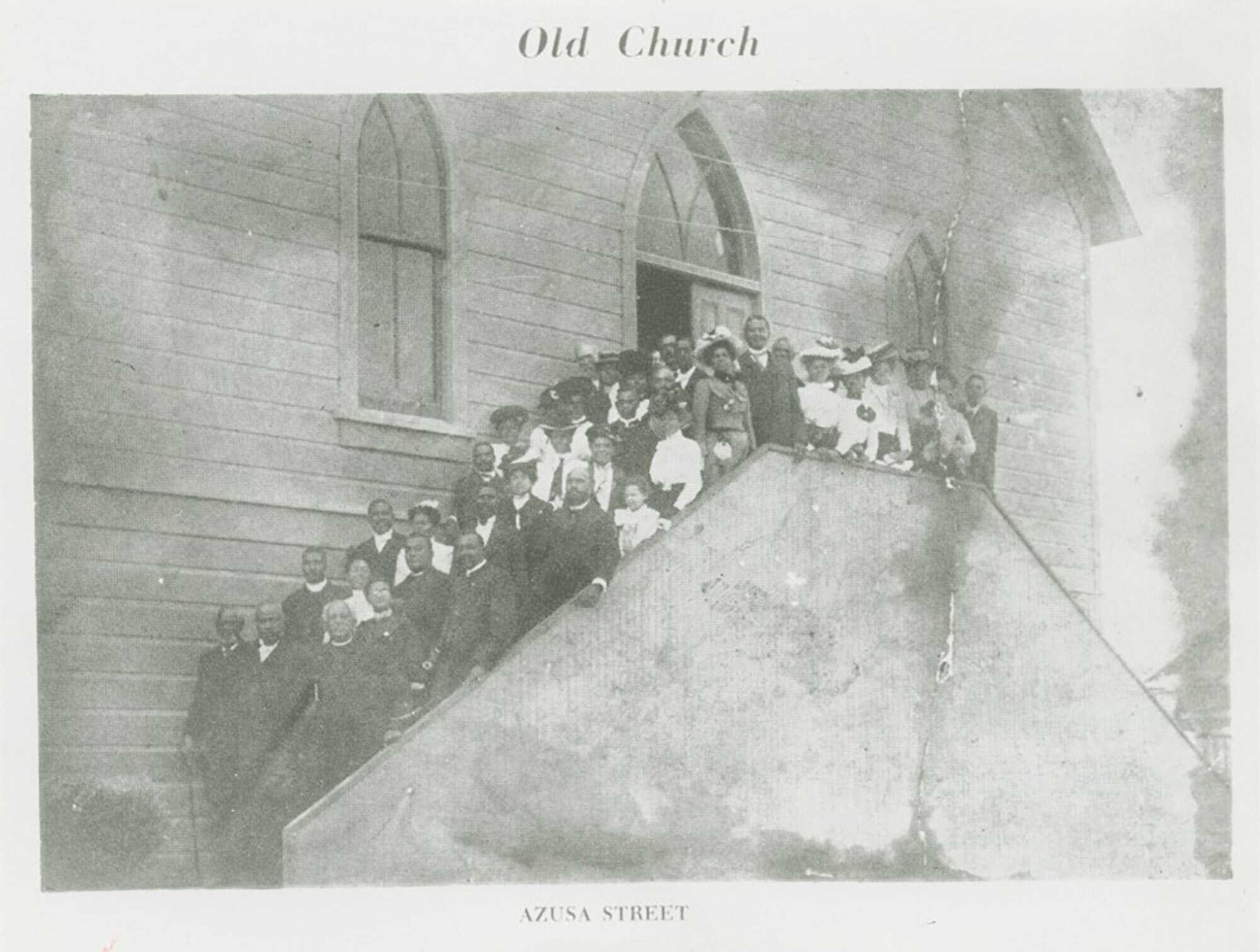 Black and white image of a copy of an image of people standing outside the steps of a church. The church exterior is wood paneling and features two (2) windows with gothic arches in the front. Between the two (2) windows, centered, is the doorway, also with a window above with a gothic arch. The arches are all divided by curved leading. The steps in the front of the building are obscured by a wall. The people stand on the steps between the exterior of the church and the exterior wall of the steps. The crowd of people are both men and women in a variety of clothes. The image is bordered in white with text centered at the top and bottom. At the top [Old Church]. Along the bottom [AZUSA STREET]. On the reverse in the lower left corner is a stamp with text and blanks to fill in. Only the last line is filled with a penned note [M. Matthews]. The stamp is four (4) lines [COLLECTION OF MIRIAM MATTHEWS/PHOTOGRAPHER/SOURCE/PLEASE CREDIT]. Along the bottom in the lower left is a penned note [AZUSA STREET CHURCH (FIRST A.M.E. CHURCH)]. In the upper right corner is the number [2] circled.