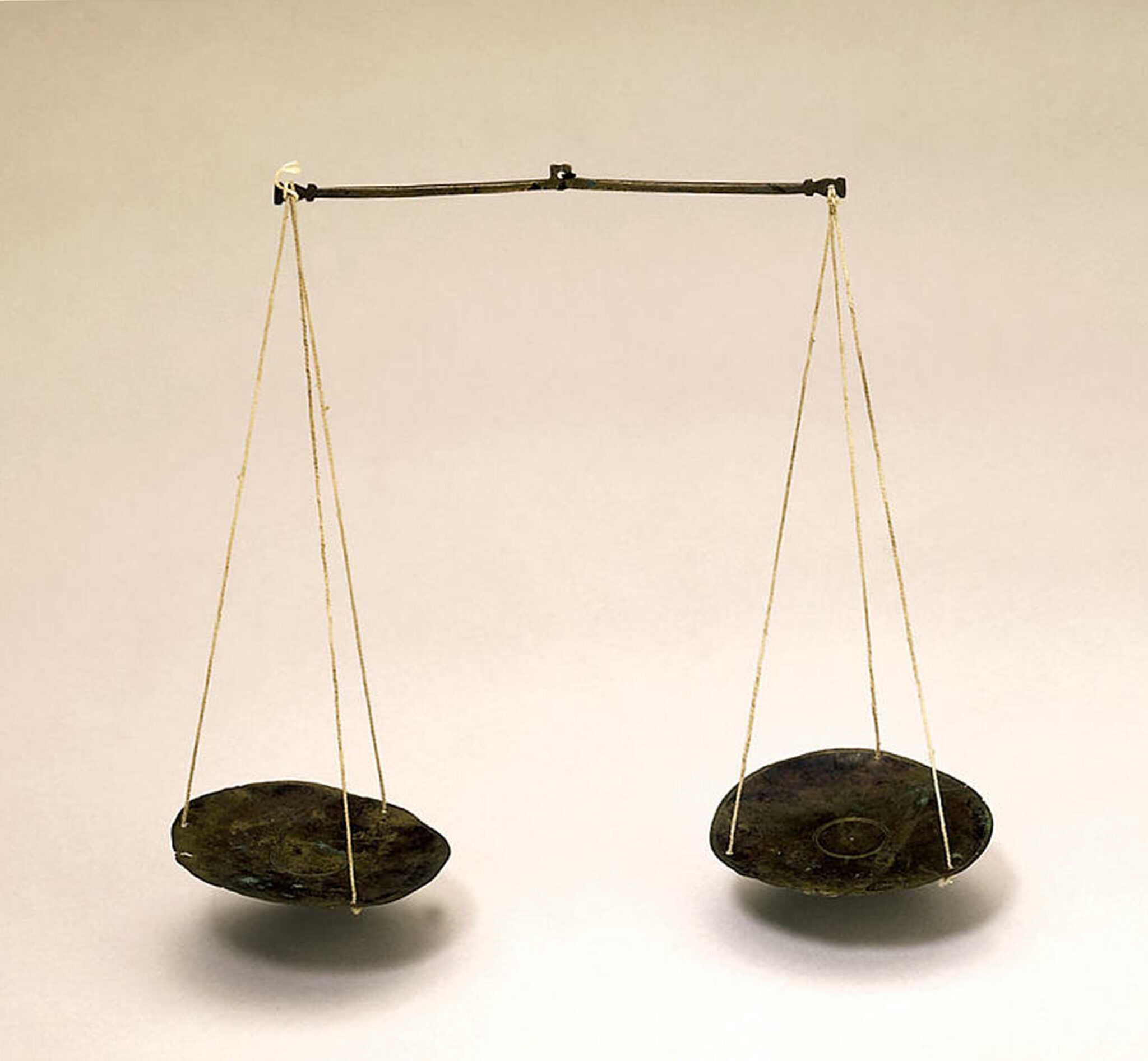 A weight scale displayed against a cream background. The scale has two plates hanging from a long metal rod.