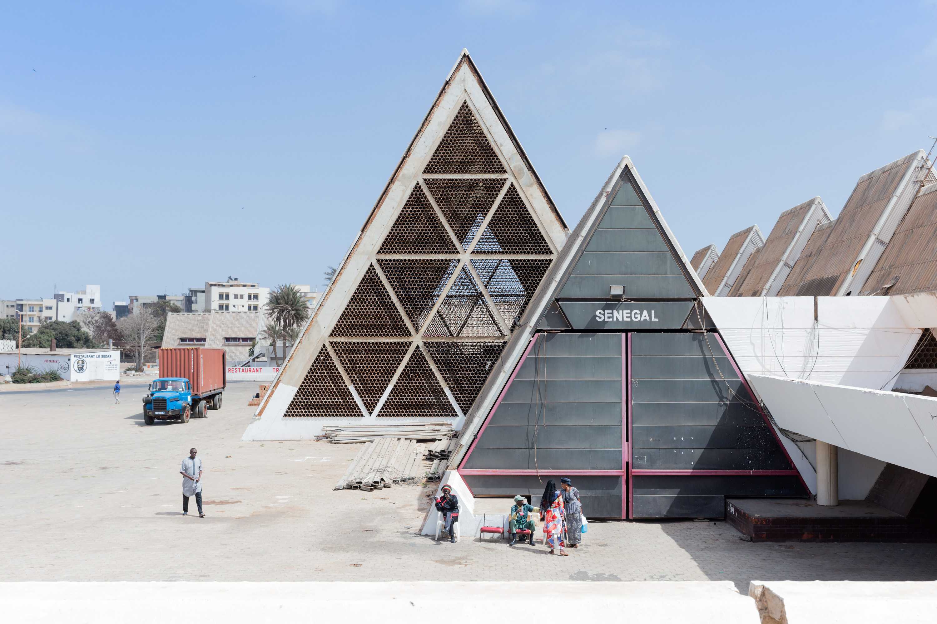 The FIDAK exhibition centre has two a-framed concrete triangles. A few people stand outside of each building.