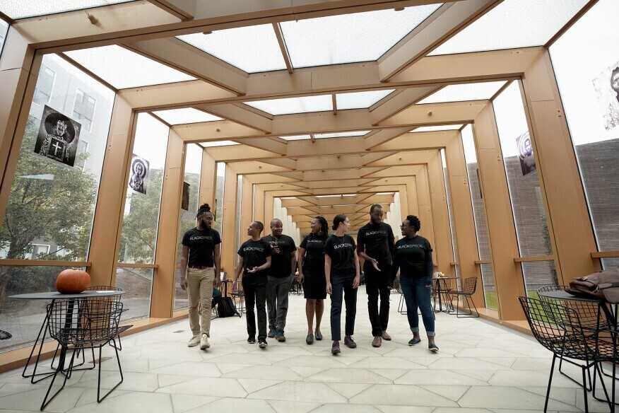 A members of the BlackSpace collective walk through an open-air halway with wooden structural columns.