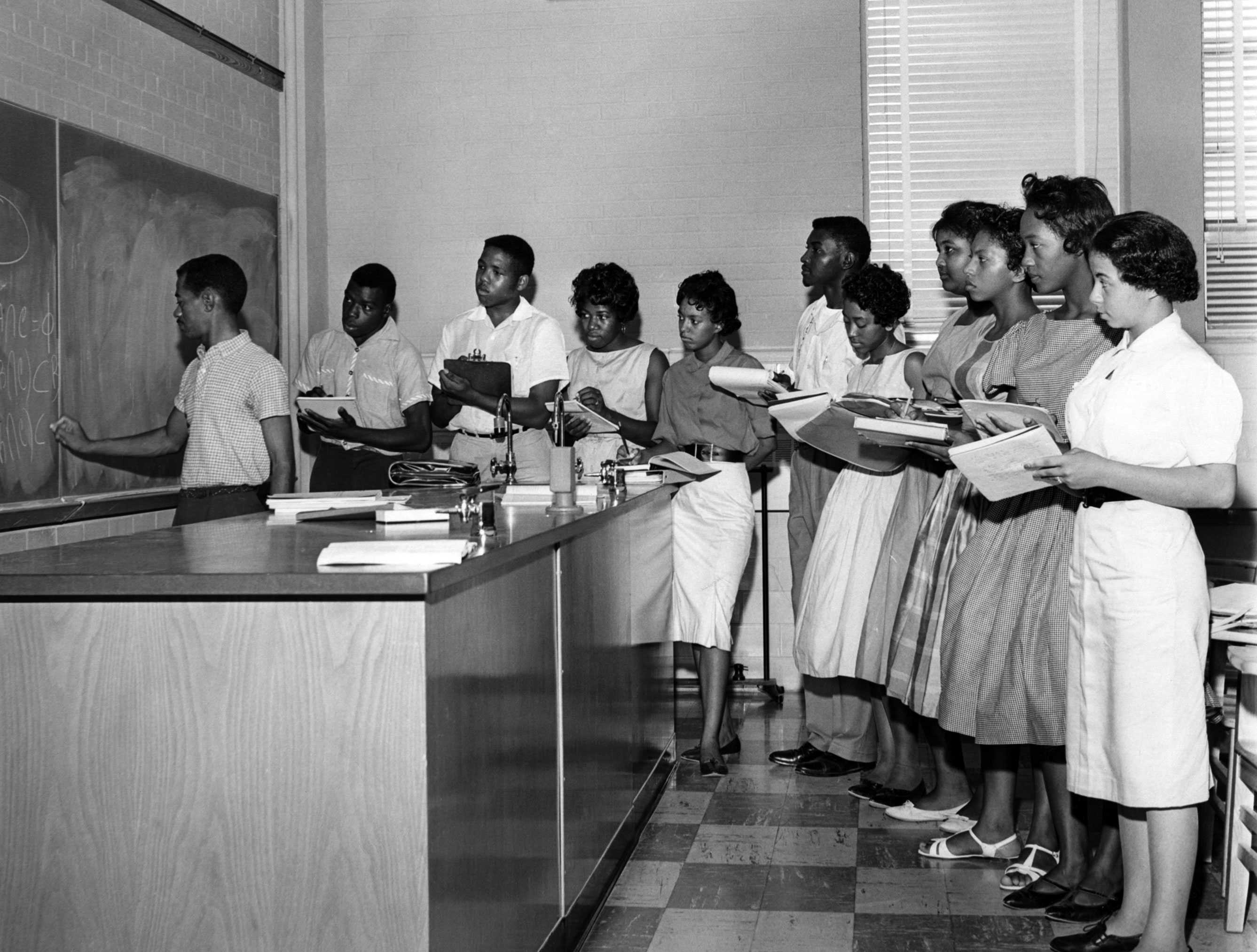 Photo of students standing at a chalkboard in a classroom, taking notes during a less